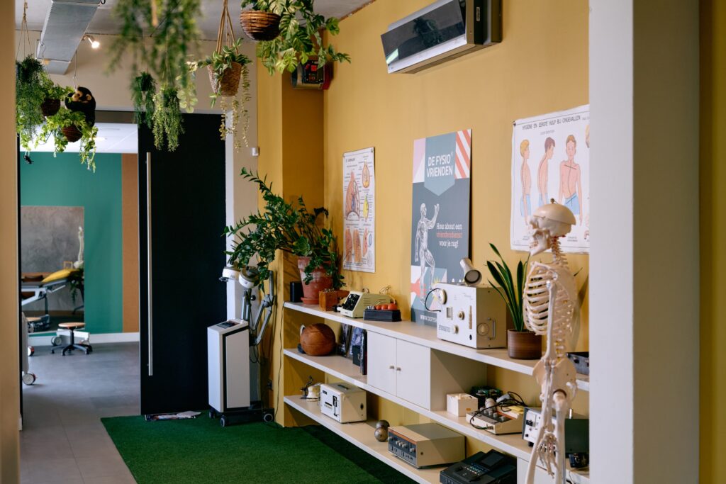 Praktijk van De Fysiovrienden met planten, een skelet en oude fysiotherapie-apparatuur tegen een gele muur